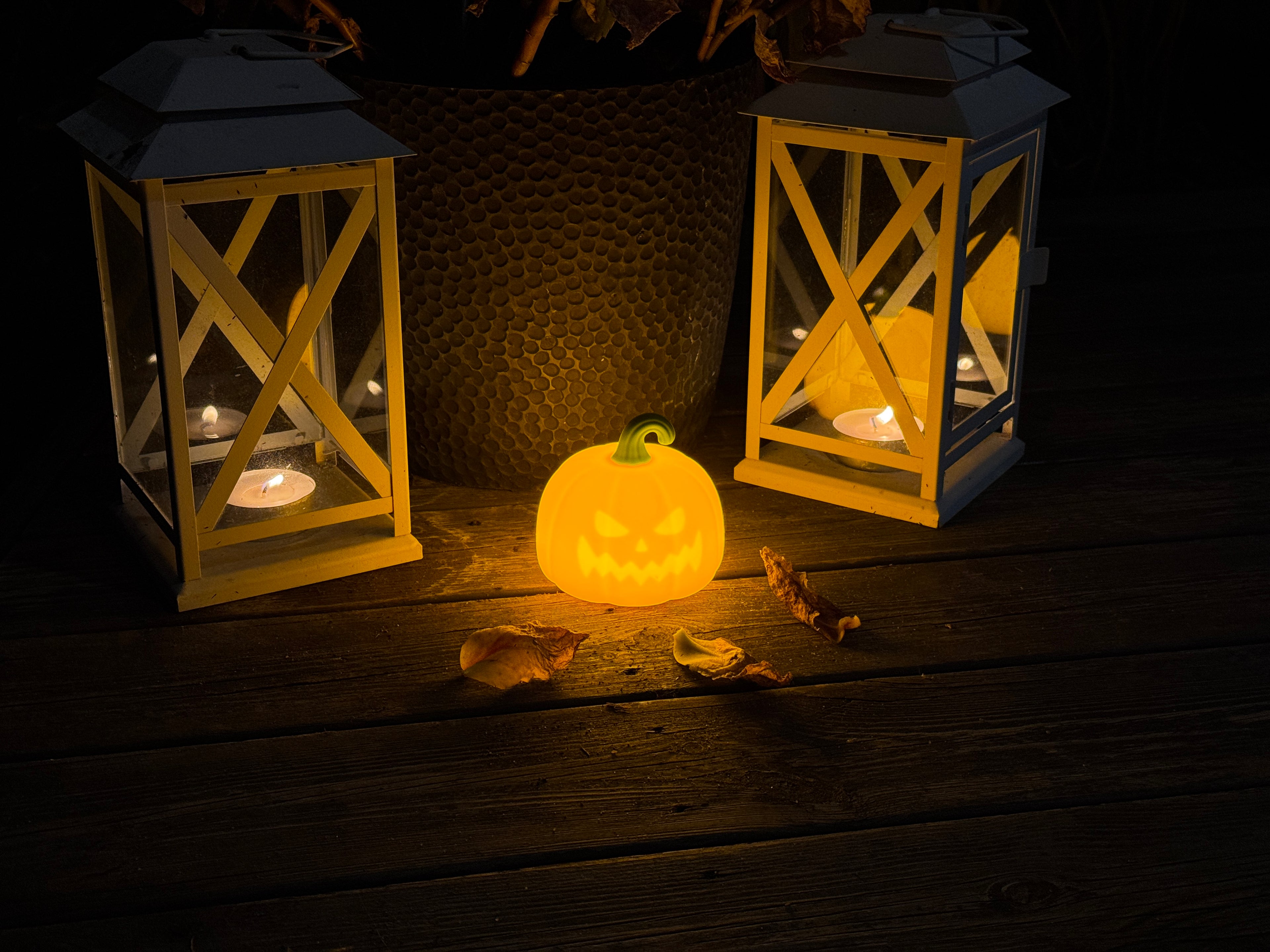 Two wooden lanterns with lit candles and a carved pumpkin on a dark wooden surface.