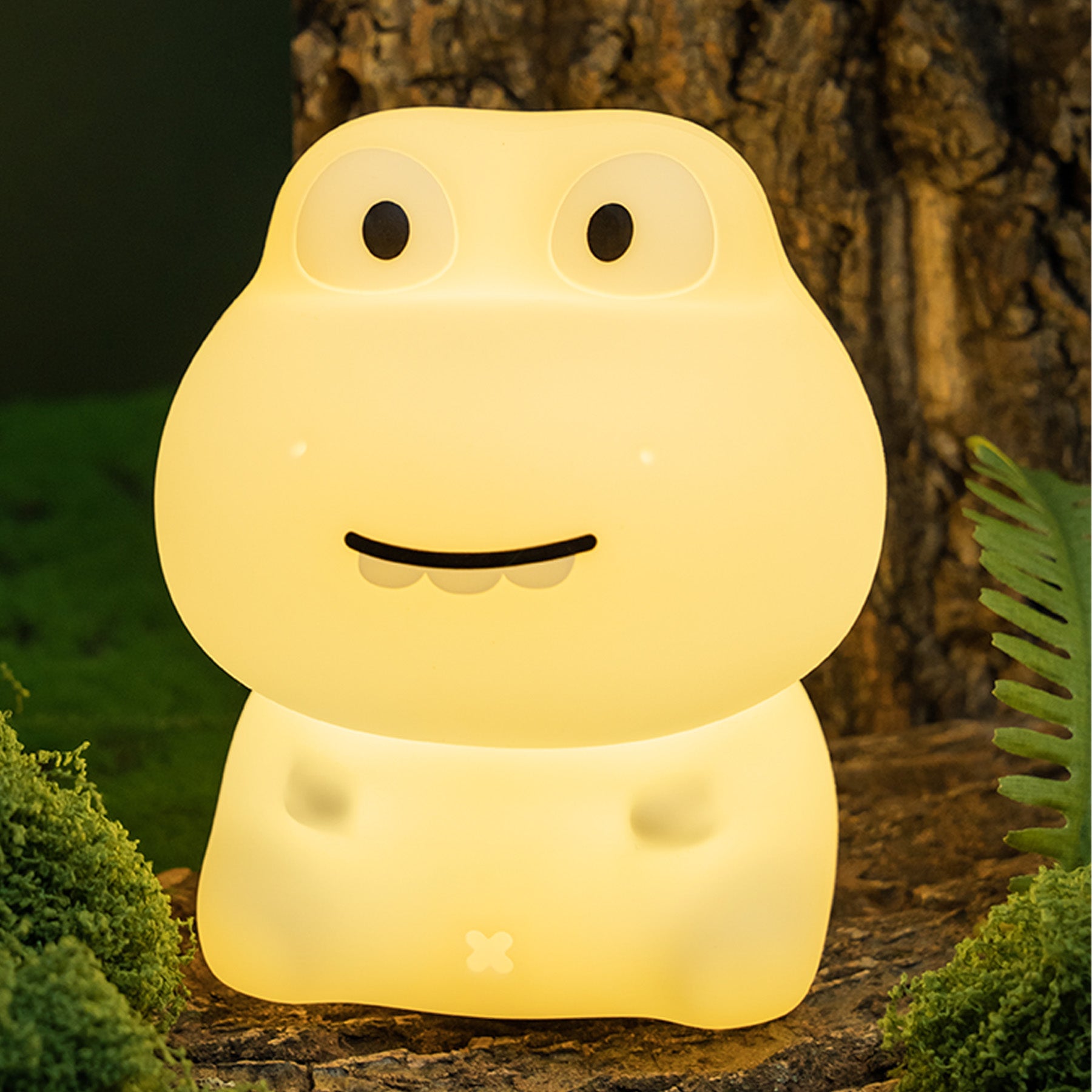 Frog-shaped night light glowing in a natural setting with trees and plants.