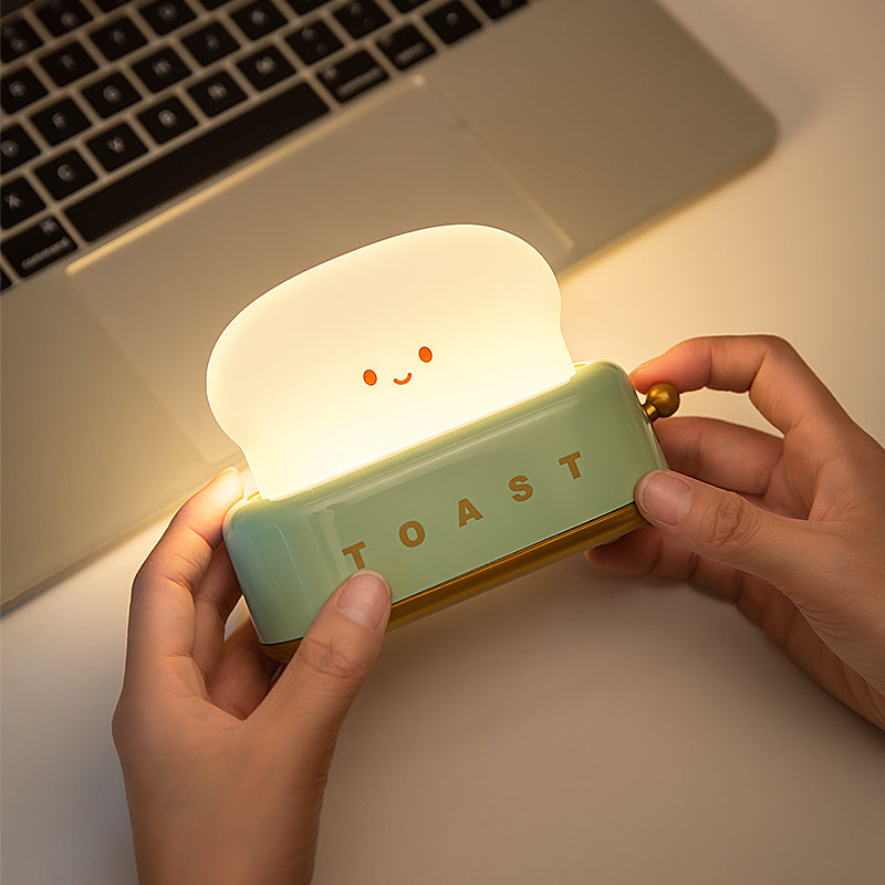 Light-up toaster shaped night light held by hands with a laptop in the background