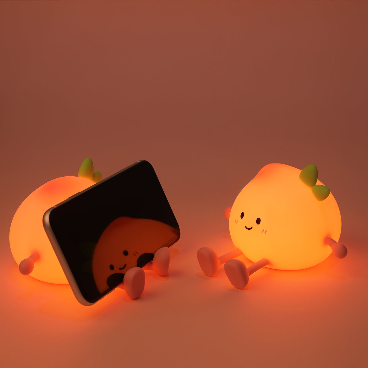 Two cute peach-shaped night lights with a smartphone on a warm brown background