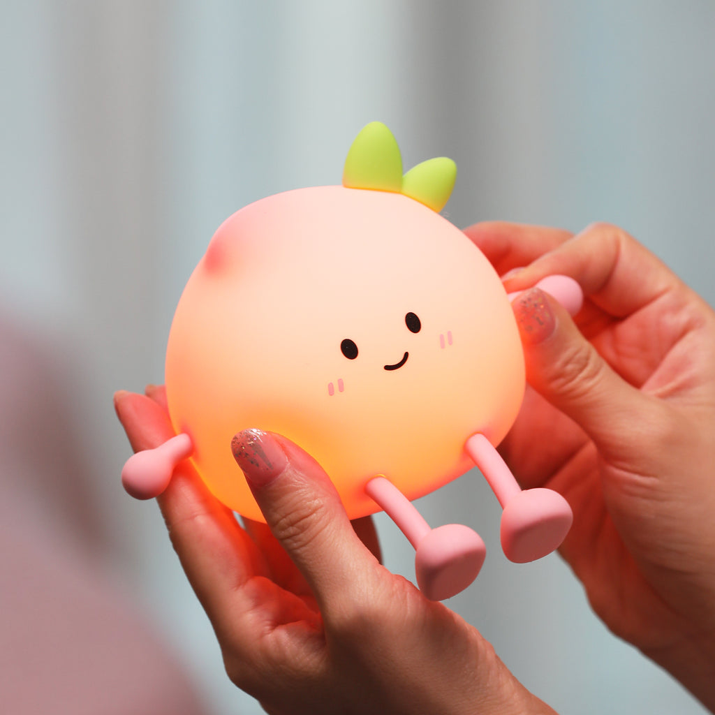 Person holding a cute, glowing fruit-shaped night light with a blurred background