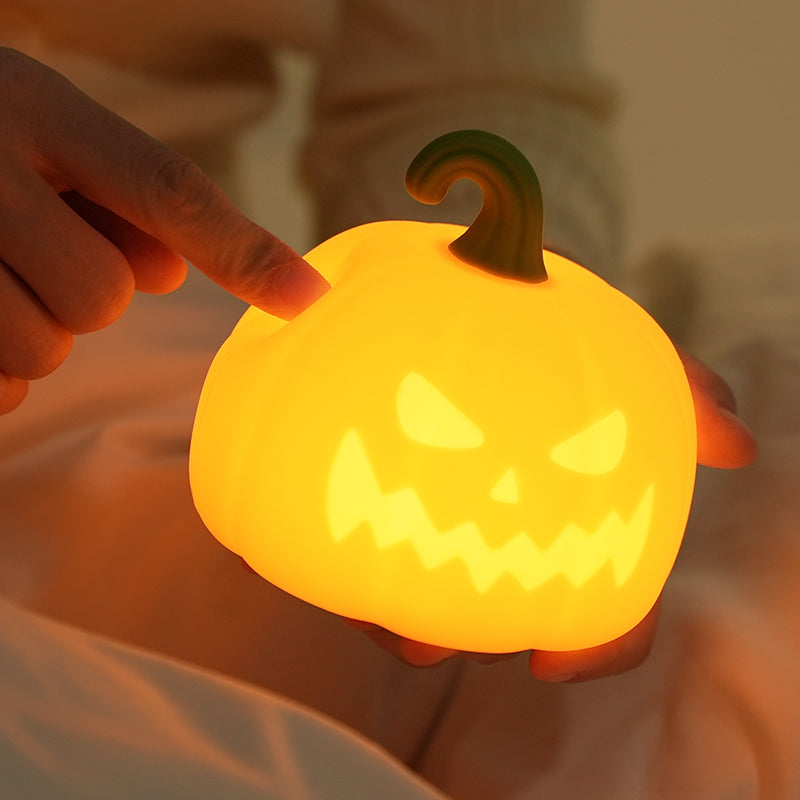 Hand holding a glowing pumpkin-shaped night light with a carved face.